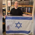 Hostage survivor Eitan Mor holds up Israeli flag of fallen soldier Yossi Hershkovitz